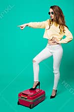 Fashionable woman in sunglasses standing on pink travel bag.