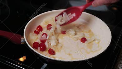Hand of a Man Stirring and Cooking Onions and Grape Tomatoes