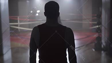Back view of confident sportsman stretching neck and walking to boxing ring. Camera follows Caucasian boxer stepping in