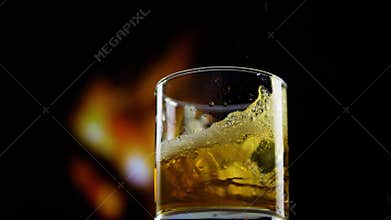 Pour whiskey into a glass,throw ice into cognac,an alcoholic drink,on a black background close-up.