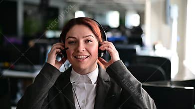 Portrait of friendly call center operator woman putting on headset in office. A smiling female hotline employee in