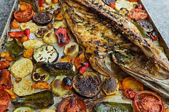 Closeup of fish baked with roasted tomatoes, potatoes and vegetables