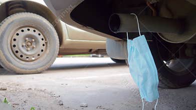 A medical mask hangs on the exhaust pipe of a car.