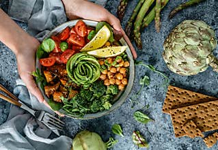Hands holding healthy superbowl or Buddha bowl with salad, baked sweet potatoes, chickpeas, broccoli, hummus, avocado, sprouts on