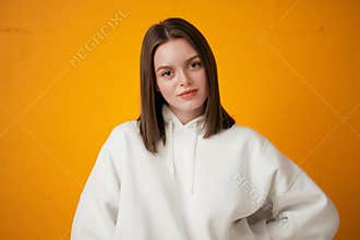 Portrait of a young pretty female student in a white hoodie, casual clothing against a concrete orange wall.