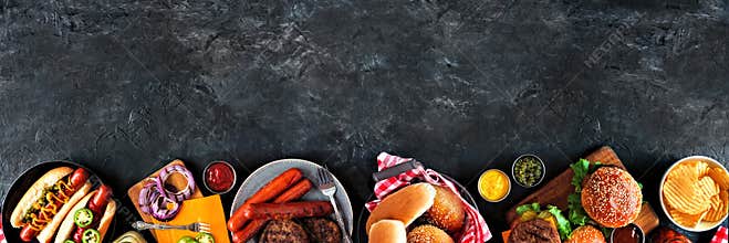 Summer BBQ food table scene with hot dog and hamburger buffet, bottom border over a dark background