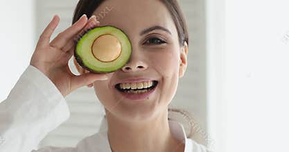 Overjoyed young pretty lady holding avocado, advertising organic cosmetics ingredients.