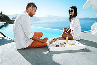 Couple on a luxury vacation in Greece, Oia Santorini men and woman at caldera infinity pool looking out over the ocean