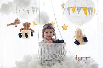Sweet toddler boy, playing with airplane and teddy bear, air balloons with toys behind him