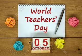 White note with inscription `World Teachers` Day` on beautiful wooden table, colored paper, metalic pen and wooden calender wit