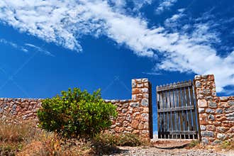 Countryside landscape. Rustic stone wall fence and aged black timber wicket door. Great blue sky with awesome clouds.
