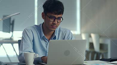 Asian creative man working on laptop. Young professional business male using computer looking information paper, business