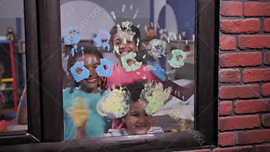 Smiling children waving painted palms at window