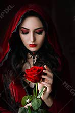 Mystical beautiful woman in a gothic costume of a medieval vampire in a hood. An adult girl holds a rose flower in her