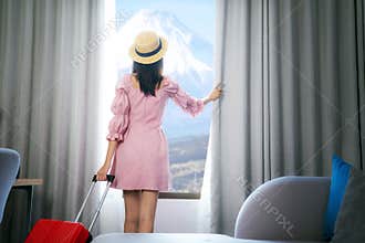 Asian woman traveller arrive to room in hotel and open curtain for enjoy fuji view