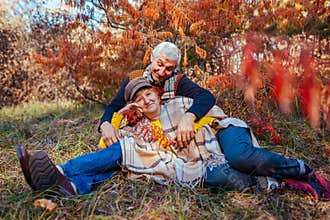 Fall family activities. Senior man and woman relaxing in autumn park lying under tree. People enjoy nature