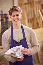 Portrait Of Male Student Studying For Carpentry Apprenticeship At College With Plans For Staircase