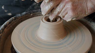 Close-up of old man`s hands working with wet clay on throwing wheel shaping vase