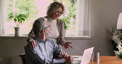 Aged spouses choosing goods discussing online purchase using laptop