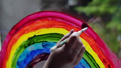 Painting a rainbow with paints on a window close-up