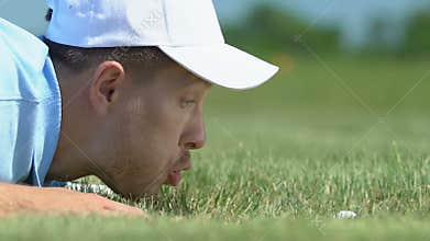 Man blowing golf ball into hole and rejoicing, breaking rules, joke, close-up