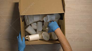 Worker in protective gloves taking box with paper cups safe cellulose utilizing