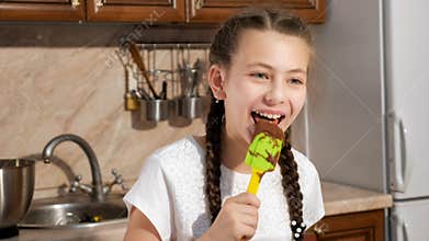 Teen girl licks plastic spatula with chocolate and smiling.