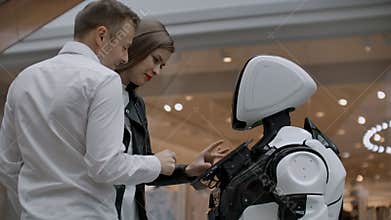 Two people a man and a woman communicate with a robot. Press the robot with your hands on the screen. A robot assistant