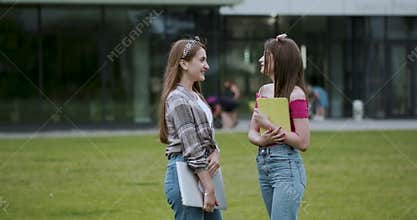 Two female college students while standing outdoors big urban building. Two teen girls talking together in the campus.
