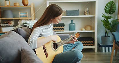 Slow motion of attractive girl enjoying music playing guitar in apartment alone