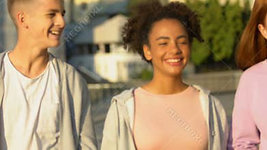 Cheerful group of young friends laughing and joking under summer sun beams