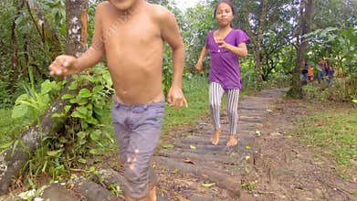 Indigenous Family Running Through A Log Path In A Amazon Village