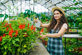 Portrait of pretty girl farmer using spray bottle in greenhouse watering flowers