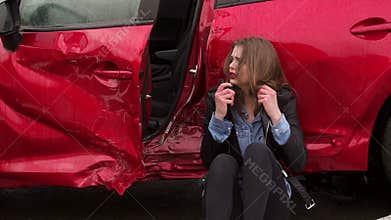 Close-up of girl sitting on the ground near a broken car, she was in an accident