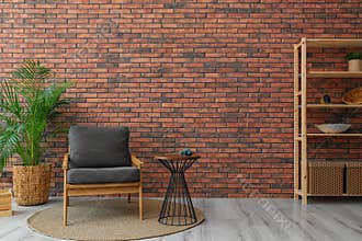 Modern room interior with stylish grey  and potted plant near brick wall
