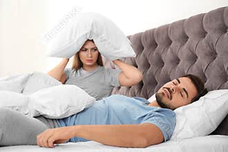 Upset young woman sitting on bed  her sleeping husband at home. Relationship problems