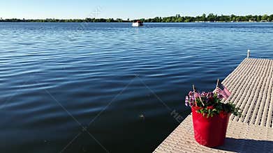 Us flags and red flowers in pot on a boat dock while a pontoon on a beautiful Minnesota lake passes by on july 4th.