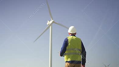 Man walking to wind mill and checking condition of mechanisms