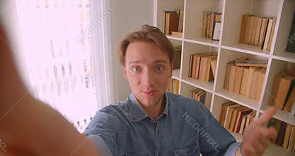 Closeup portrait of young handsome caucasian male blogger streaming live in library indoors