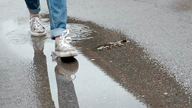 Closeup of female legs in jeans and sneakers. Walking through the puddles on a rainy day.