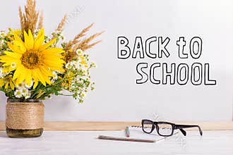 The inscription marker on a white board, Back to School. A table with a bouquet of flowers, glasses and attributes for writing