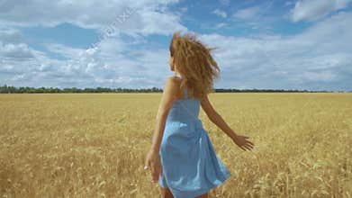 Happy young girl runs in slow motion across field, touching ears of wheat with her hand. Beautiful free woman enjoying