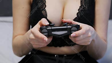 Close-up shot of sexy unrecognizable woman in a lace bra with gorgeous breasts playing games on the console on gamepad
