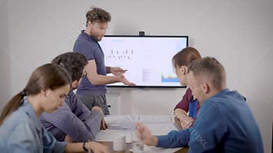 Man is presenting financial report at meeting with colleagues in conference hall of office, showing charts