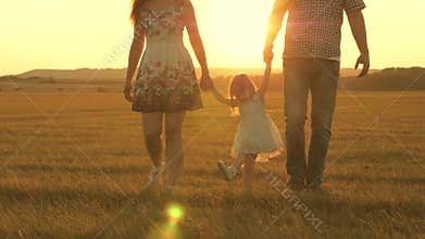 Little daughter jumping holding hands of dad and mom in park on background of sun. Family concept. child plays with dad
