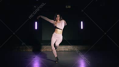 Portrait of sexy girl in pink tight-fitting suit sensually dancing dark studio