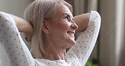 Happy dreamy older woman relax hands behind head at home