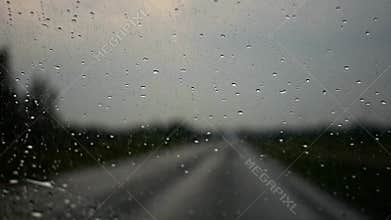 Rain drops on the car windshield. Heavy rain on the street, moving car in the evening - dangerous weather conditions.