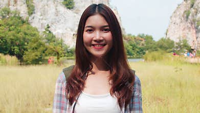 Cheerful young traveler Asian lady with backpack feeling happy smiling to camera at mountain lake. Korean girl enjoy her holidays