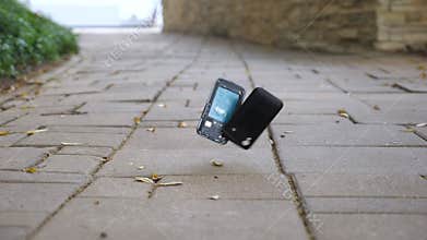 Outdated black smartphone falls on grey pavement and crashes